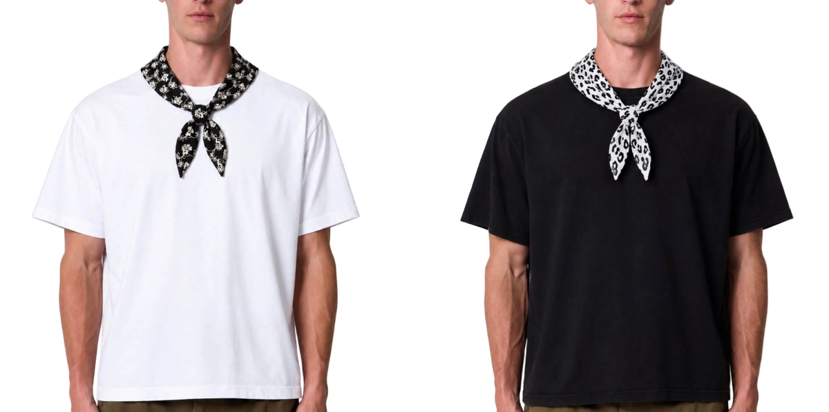 Two male models wearing short-sleeve crew-neck t-shirts, one white and one black, each styled with a black-and-white patterned neck scarf tied at the collar, against a plain white background.